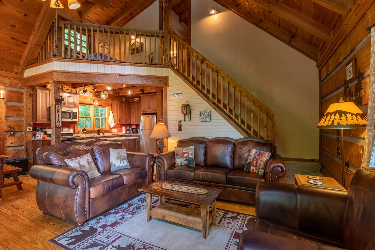 This photo focuses on the open-concept living area, highlighting the leather sofas and wooden coffee table with a partial view into the kitchen. The staircase and kitchen area are visible in the background, reinforcing the seamless flow between spaces for both relaxation and entertaining.