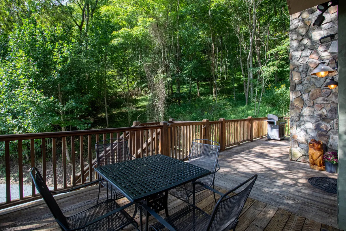 A tranquil scene of a wooden deck with a metal table and chairs, bordered by a stone wall and enveloped by natural greenery. This inviting space suggests opportunities for outdoor dining, barbecues, or simply taking in the fresh mountain air with friends—directly supporting the idea of group relaxation and adventure.