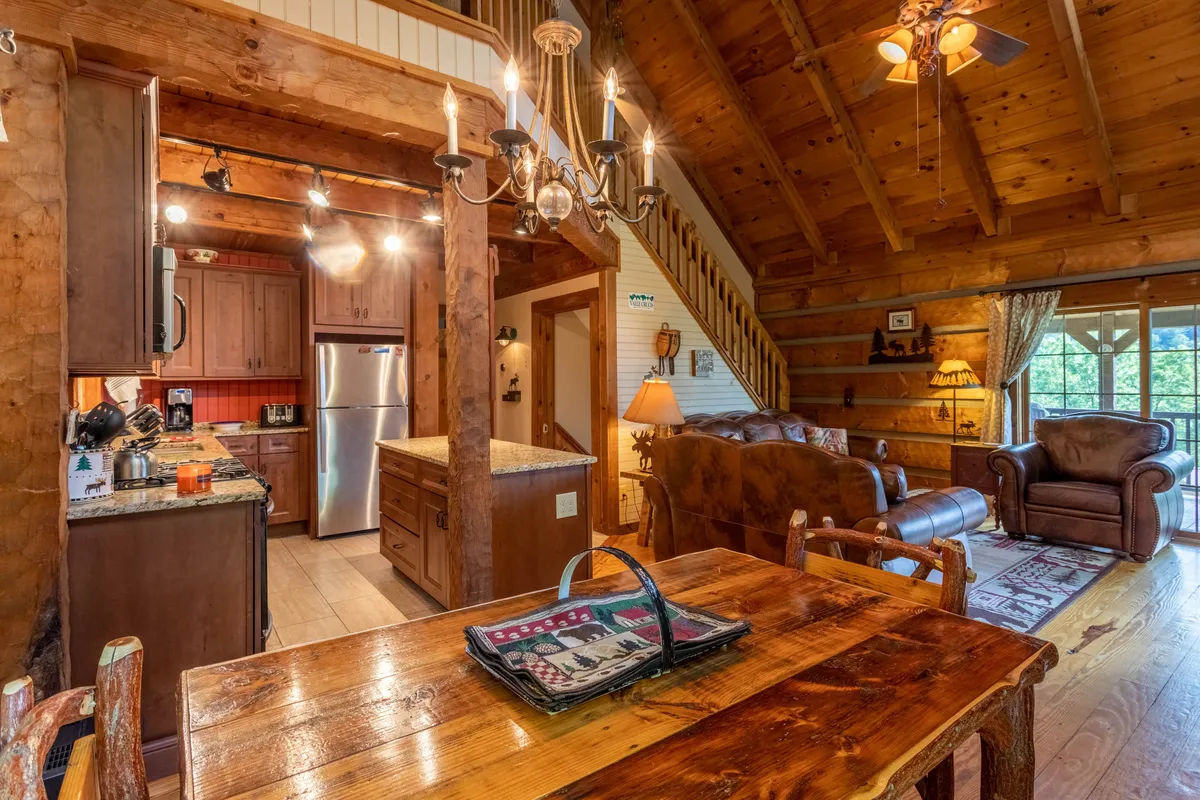 A warm and inviting dining and lounge area with a wooden dining table under a chandelier, leather couches, and expansive windows. The space encourages intimate gatherings and quiet mornings, with plenty of natural light and a view that hints at the beauty of the surrounding landscape.