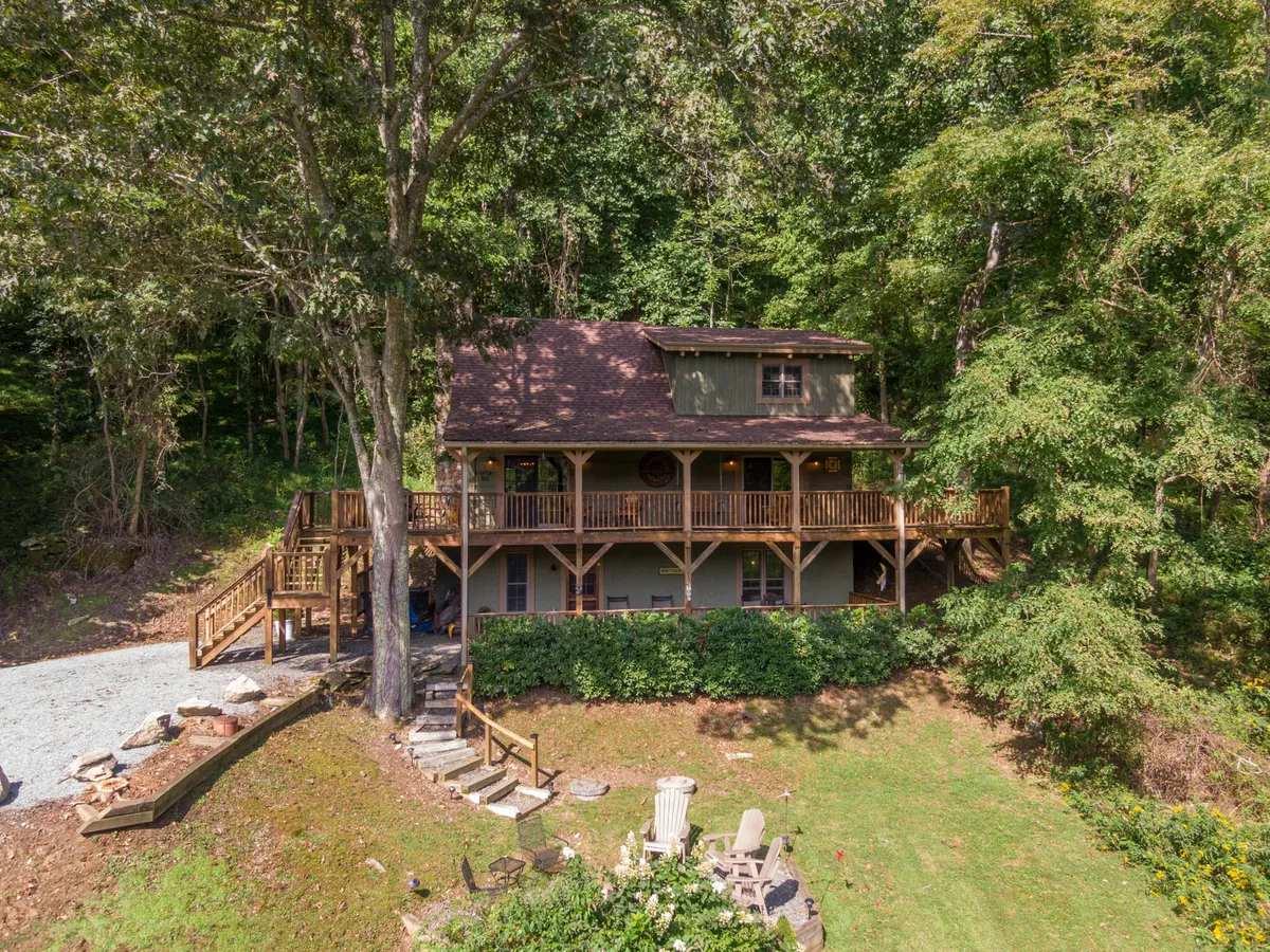 A wooden deck bordered by lush greenery, with a stone pathway leading to a cozy seating area. The scene suggests opportunities for family barbecues, stargazing around the fire pit, and peaceful mornings with coffee on the porch, all in the embrace of nature.