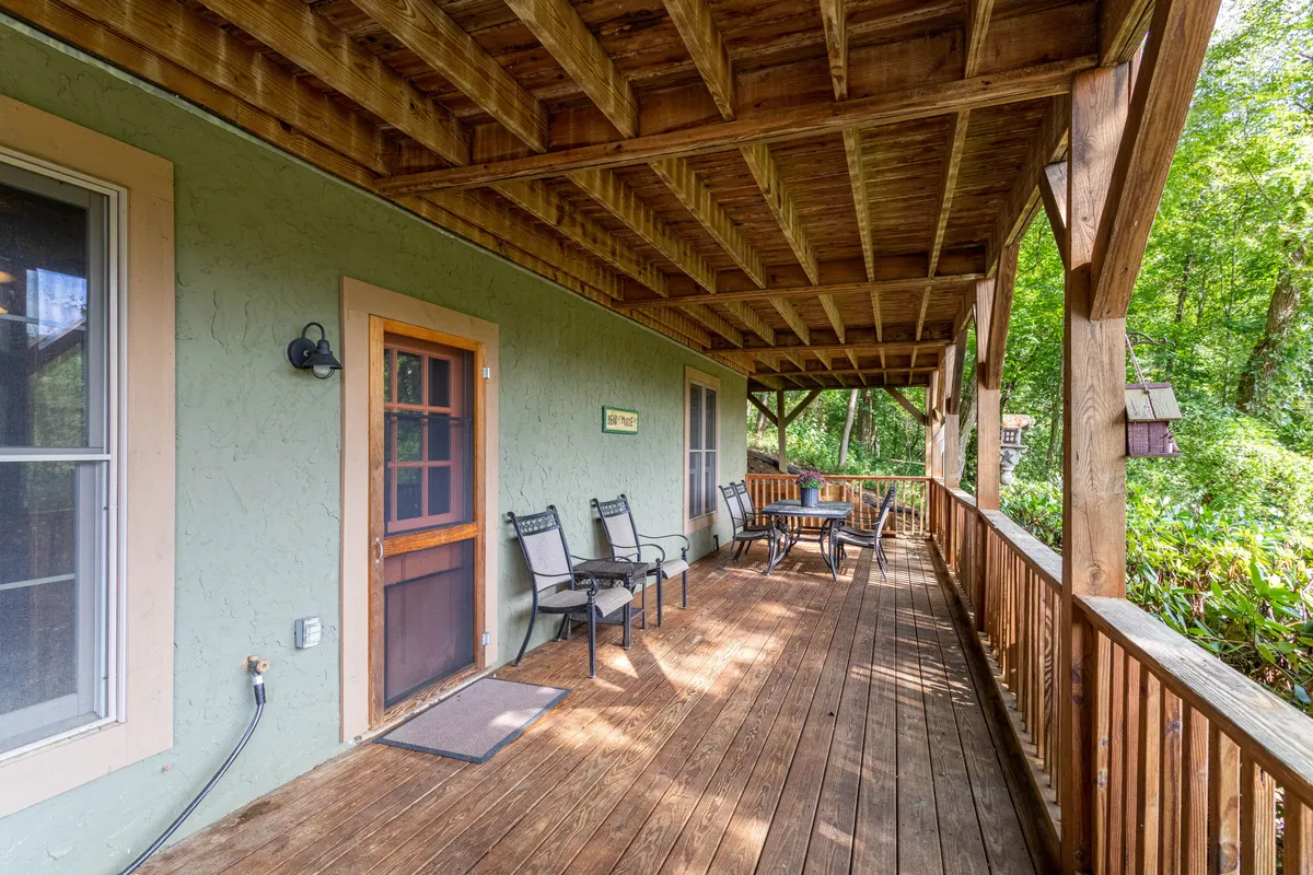 This image showcases a spacious wooden deck attached to the cabin, featuring a comfortable seating area and a green exterior wall, all surrounded by a backdrop of lush natural scenery. The setting welcomes outdoor relaxation while providing direct access to the beautiful mountain environment.