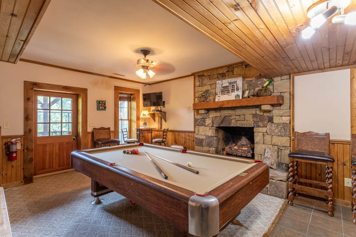 Another angle of the game room, showing the pool table, a welcoming fireplace, and adjacent wooden furniture. The doorway hints at direct access to other parts of the house, reinforcing the idea of connected spaces for seamless flow between activities. The room exudes warmth and friendliness, ideal for socializing.