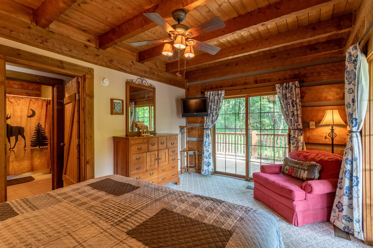A warm, inviting living space with a comfortable red couch positioned near a large window that overlooks a balcony, allowing guests to enjoy the beautiful mountain scenery from inside or step out to embrace the outdoors.