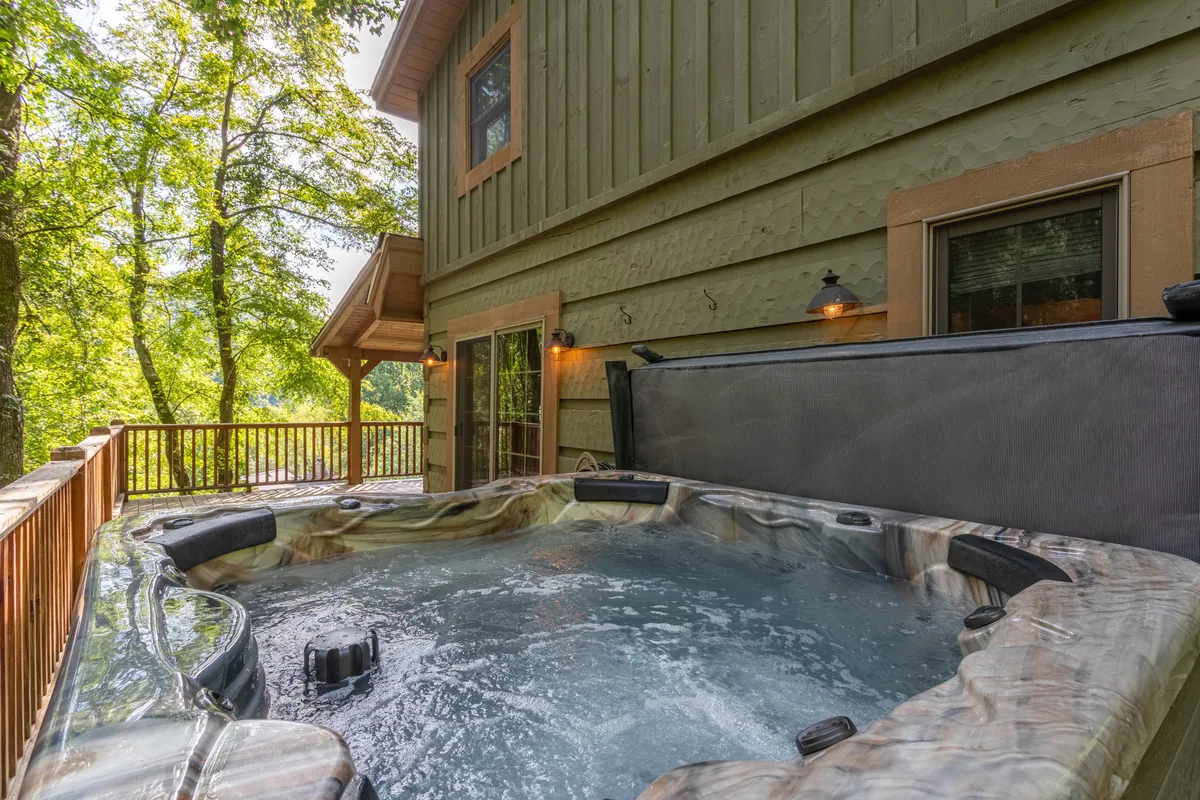 A close-up view of the hot tub set on the deck, surrounded by trees and natural mountain greenery, emphasizing the peaceful, private spa experience available at the property.