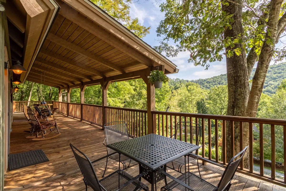 A panoramic shot of the deck featuring rocking chairs, a dining table, and lush greenery, with expansive views toward the mountains. The space is designed for lounging, outdoor dining, and taking in scenic vistas.
